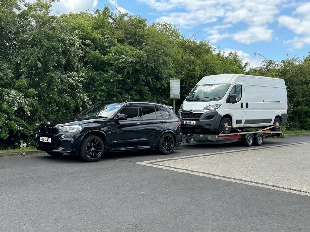 A BMW X5 towing a white van on a trailer