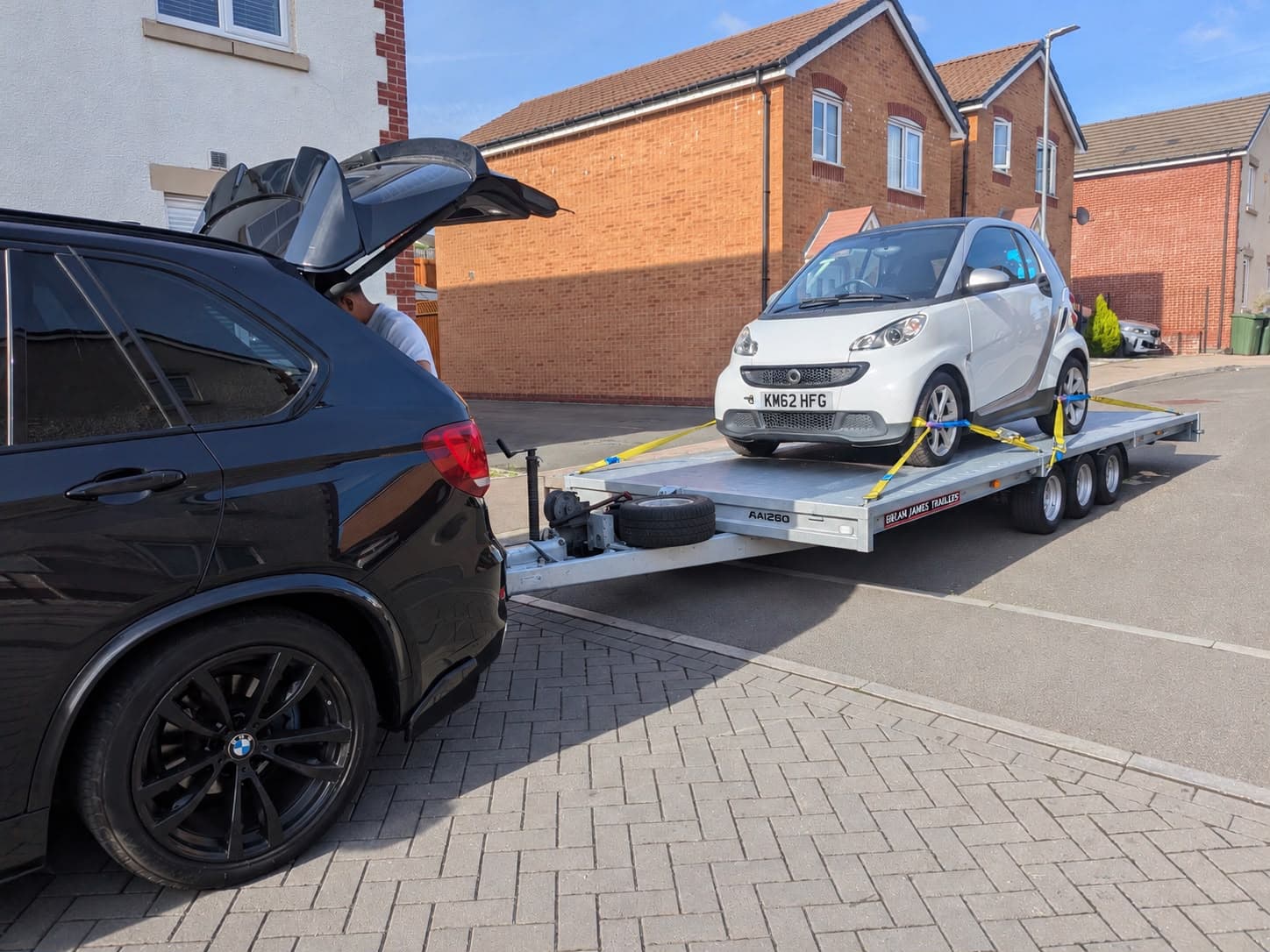 A BMW X5 towing a white Smart car on a trailer