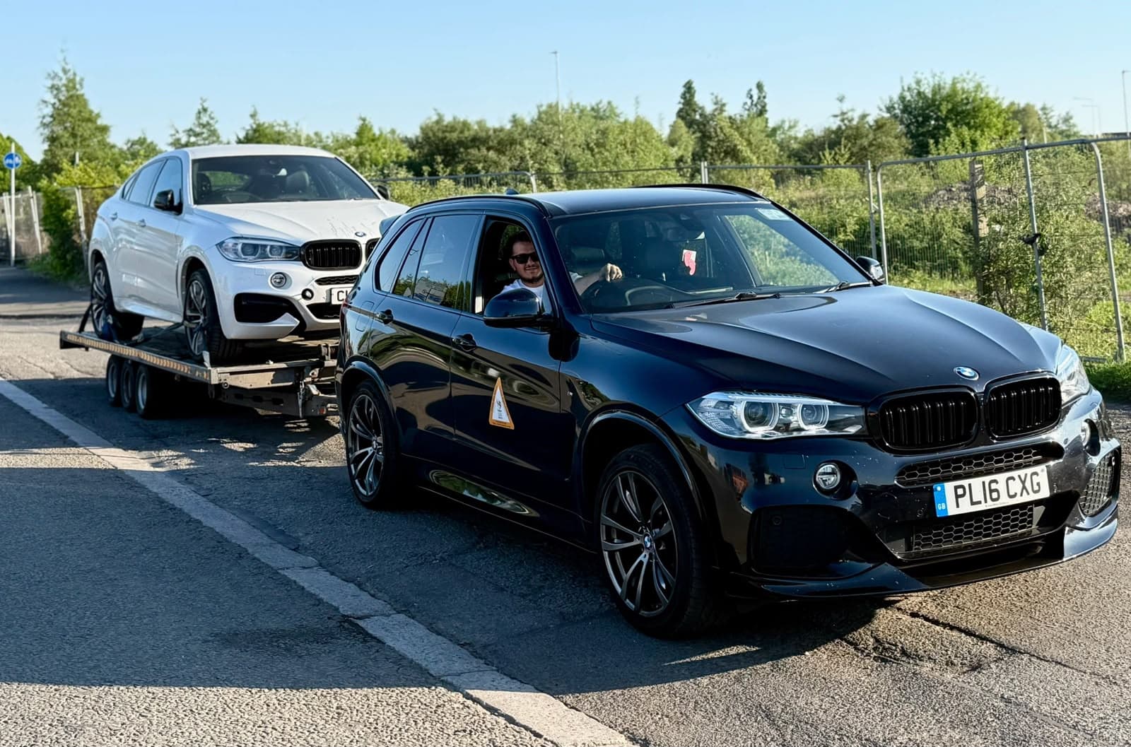 A black BMW X5 towing a white BMW X6 on a recovery trailer